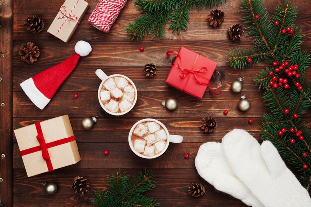 Фото Две чашки горячего какао или шоколада с маршмелло подарки белые рукавицы рождественский декор и пергамент