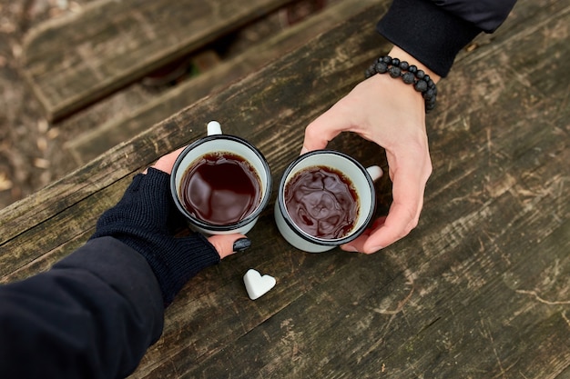 Две чашки чая на природе в руках пары в черных перчатках на деревянной поверхности
