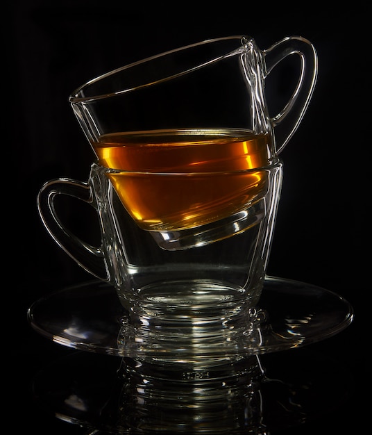 Two cups standing one in another with tea on a black background with reflection