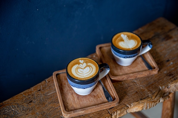 Two cups of tasty cappuccino with latte art on wooden table background. Top view on blue background