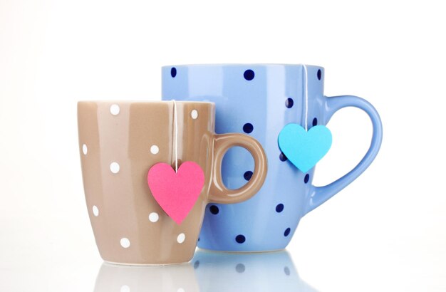 Two cups and tea bags with red and blue heart-shaped label isolated on white