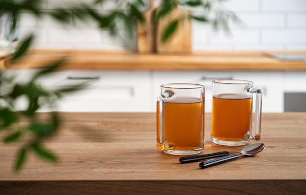 Due tazze di tè e foglie per il brunch si chiudono su un piano di lavoro in legno sullo sfondo di una cucina bianca al mattino presto concetto di colazione sana