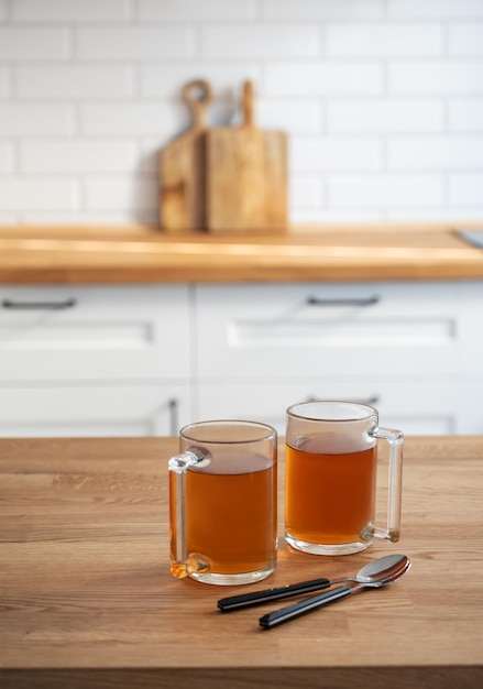 Two cups of tea on a wooden countertop against the background of a white kitchen in the early morning Healthy breakfast concept Copy space Vertical orientation