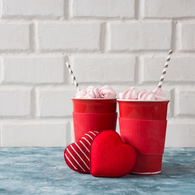 Two cups with coffee and marshmallow and two knitted hearts, concept of Valentine's Day ho