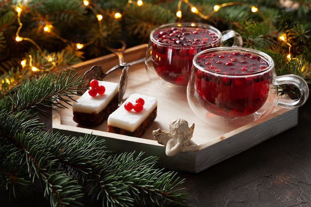 Two cups with hot Christmas spicy drink with cranberry and cakes