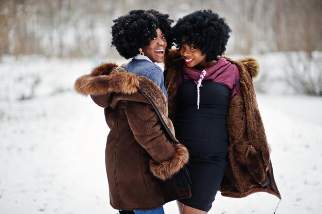 Two curly hair african american woman wear on sheepskin coat and gloves posed at winter day