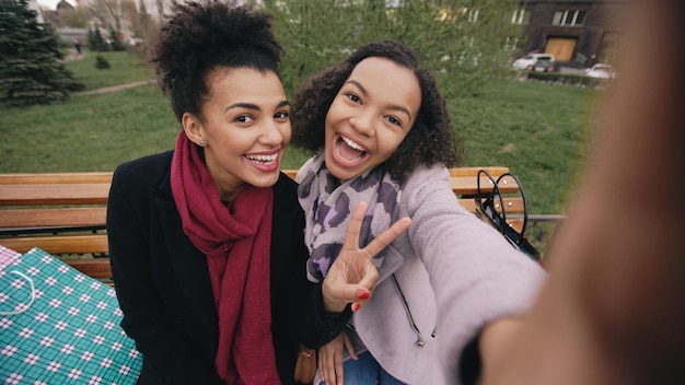 Photo two cute african american woman taking selfie on smartphone with shopping bags and smiling