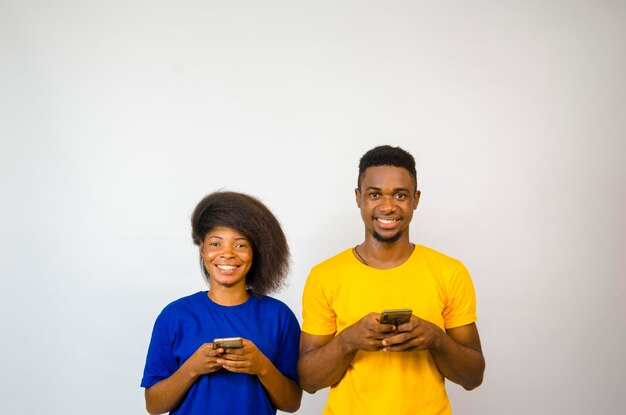 Two cute africans standing side by side isolated over white background smiles as they operate their cellphone