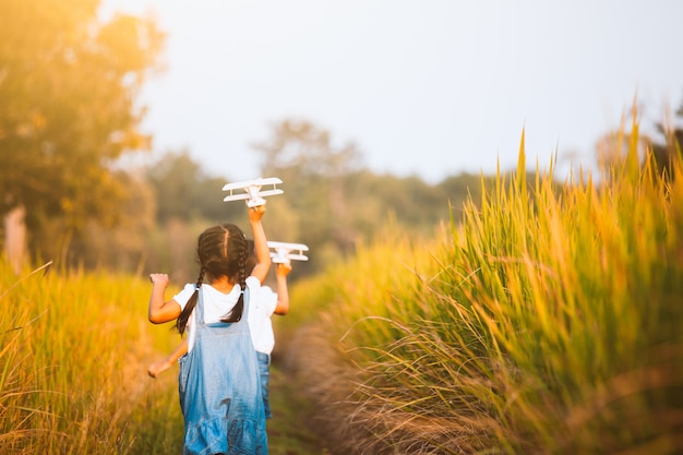 Two cute asian child girls running and playing with toy wooden airplane in the field