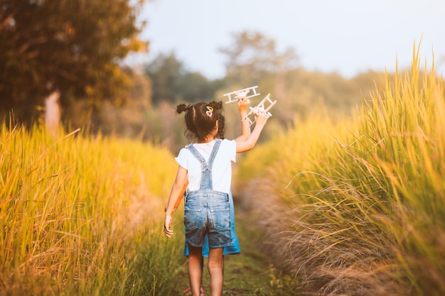 Two cute asian child girls running and playing with toy wooden airplane in the field