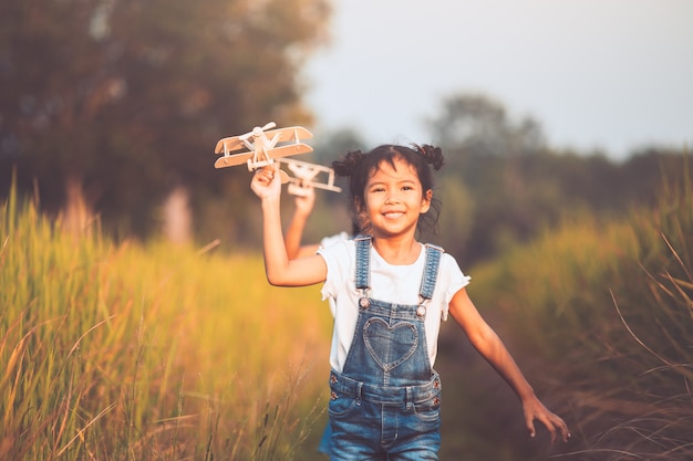 Two cute asian child girls running and playing with toy wooden airplane in the field