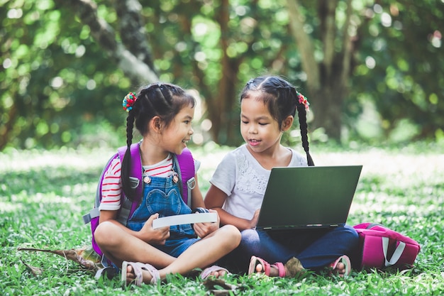 Two cute asian child girls using laptop in the park together with fun and happiness.