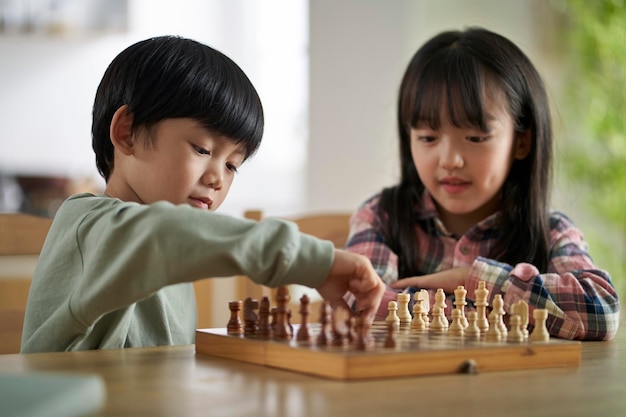 двое милых азиатских детей брат и сестра играют в шахматы дома