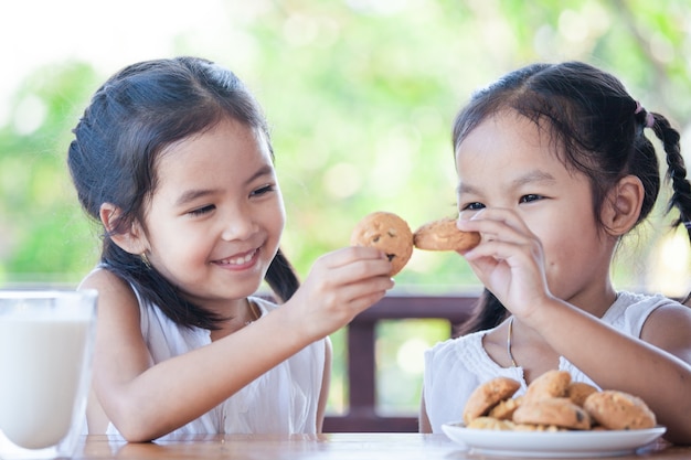 Two cute asian little child girls are eating cookies with milk for breakfast