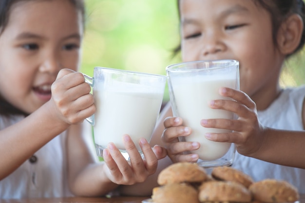 Photo two cute asian little child girls holding glass of milk for breakfast