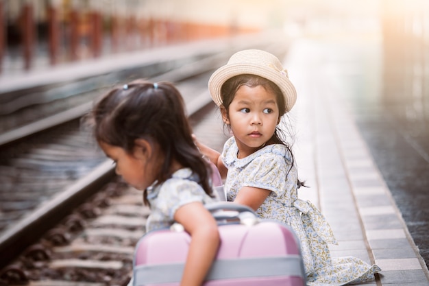 Two cute asian little girls waiting for the train with suitcase