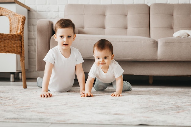 Two cute babies in white tshirts crawl and play on the floor of the house two brothers