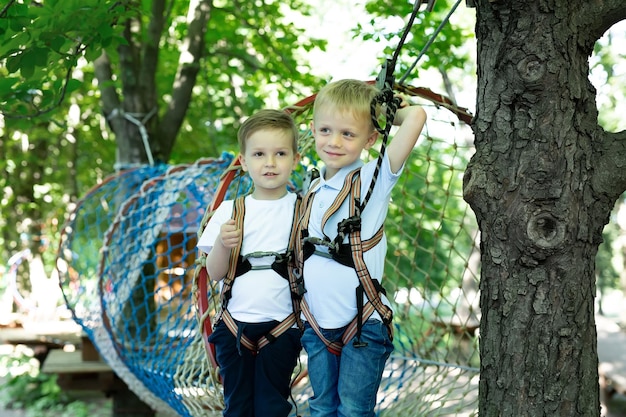 Two cute boys in an adventure park are doing rock climbing or passing obstacles on a rope road