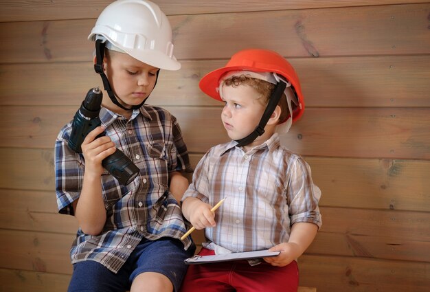 Two cute boys in construction helmets are discussing a plan for the upcoming work. children play builders. little boy with a screwdriver in his hands