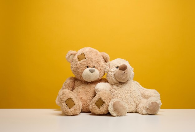 two cute brown teddy bears sitting on a yellow background childrens toy