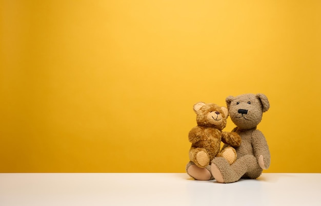 Two cute brown teddy bears sitting on a yellow background, childrens toy