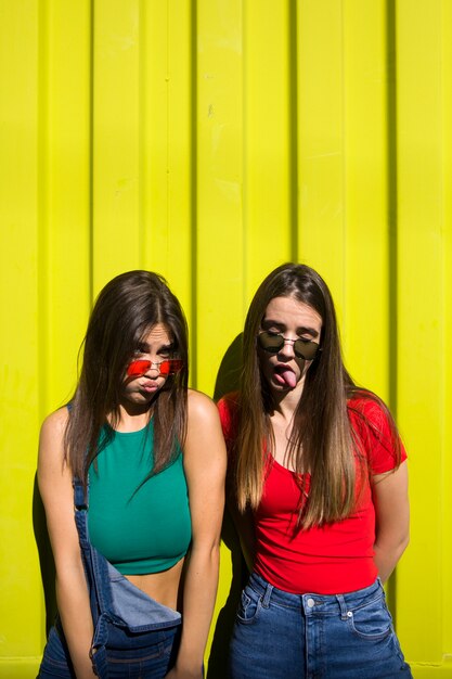 Two cute casual young women fooling around in front of yellow wall