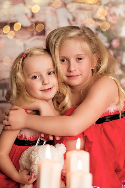 Two cute cheerful girls in Christmas clothes against the background of the Christmas tree