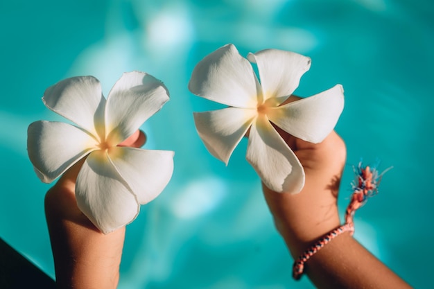 Two cute children's hands are holding plumeria flowers on a background of water, close up