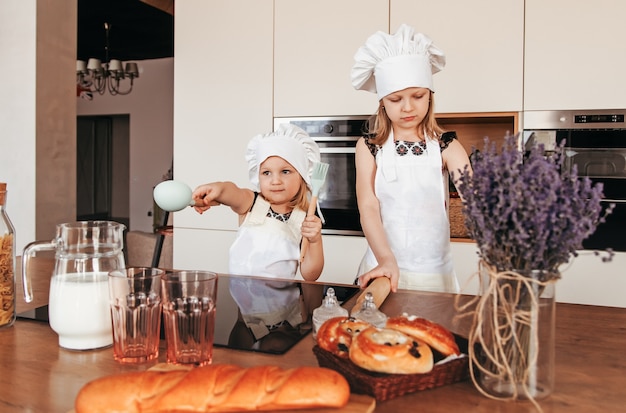 Two cute girls in chef hats and white aprons cook in the kitchen.