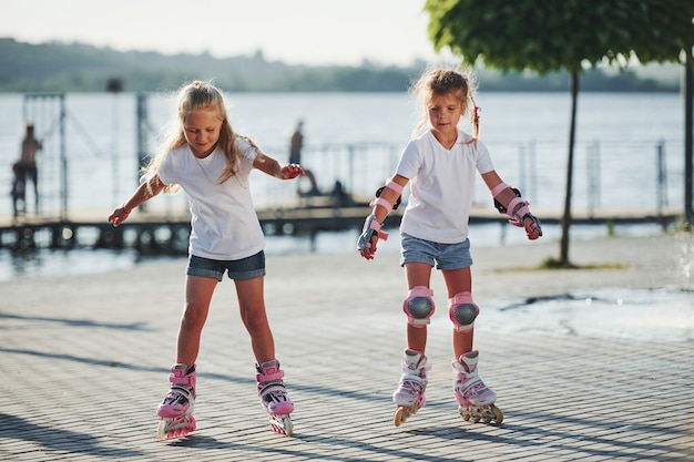 Two cute kids riding by roller skates in the park at daytime.