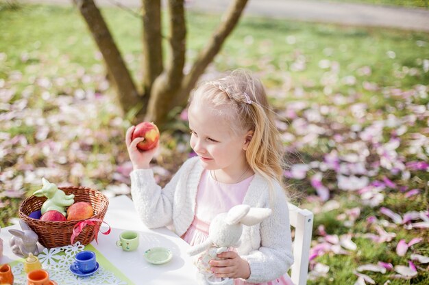 Two cute little blonde girls of 3 years old are playing in the\
park near a blossoming magnolia. tea drinking. easter. spring.