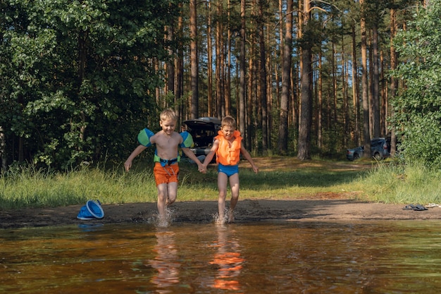 two cute little boys running into lake splashing water in the forest