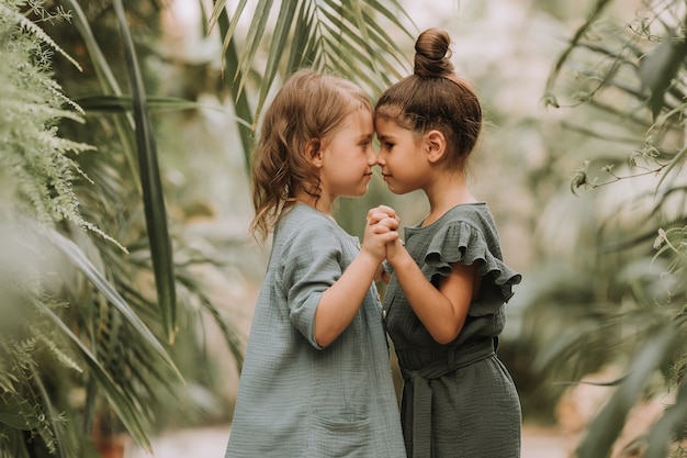 Two cute little girls belonging to different races holding hands and walking in botanical garden