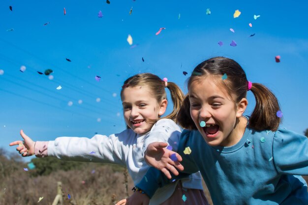 Two cute little girls celebrating and playing with confetti. they are in a field with a blue sky