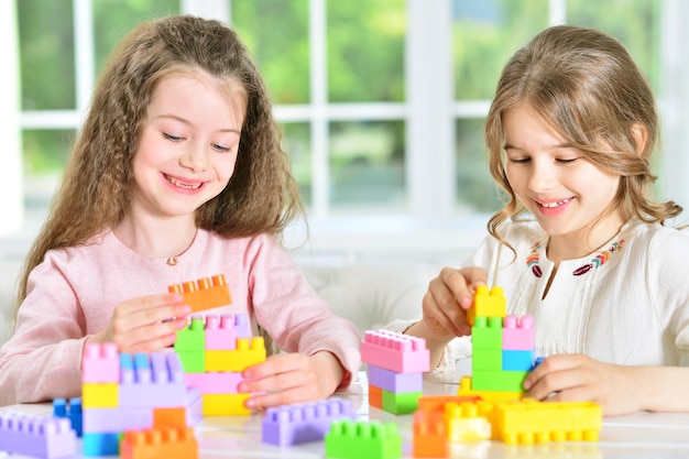 Two cute little girls playing with colorful plastic blocks