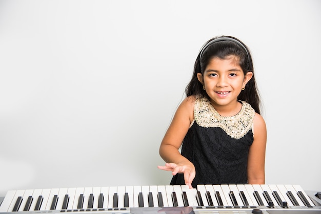 Due simpatiche ragazze indiane o asiatiche che suonano il pianoforte o la tastiera, uno strumento musicale, su sfondo bianco