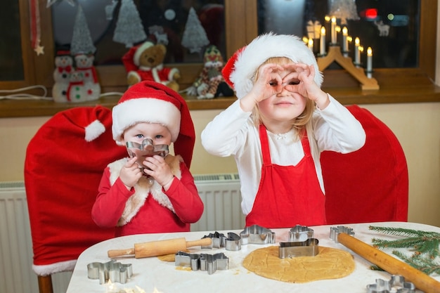 Two cute little sisters are cooking christmas cookies in cozy home kitchen