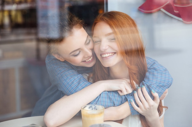 Two cute lovely happy young women hugging in cafe