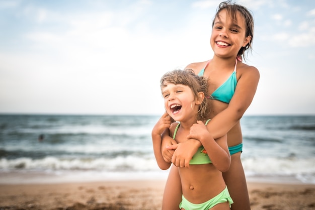 Two cute positive little girls sisters raised their hands up while swimming at sea