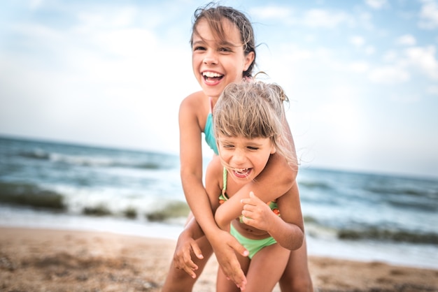 Two cute positive little girls sisters raised their hands up while swimming at sea