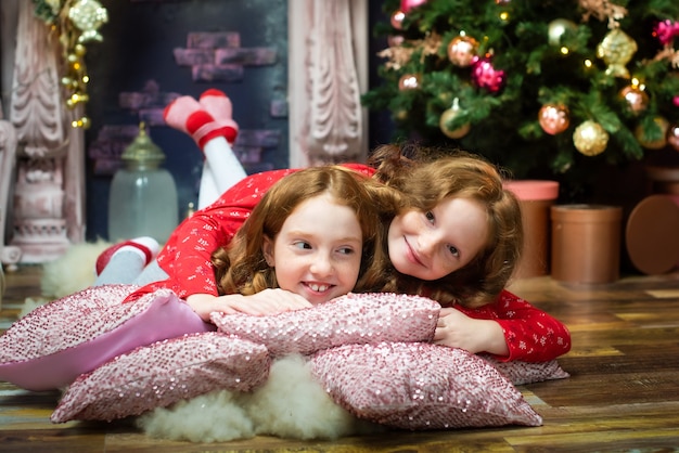 Two cute redhead sisters open presents by the new year tree