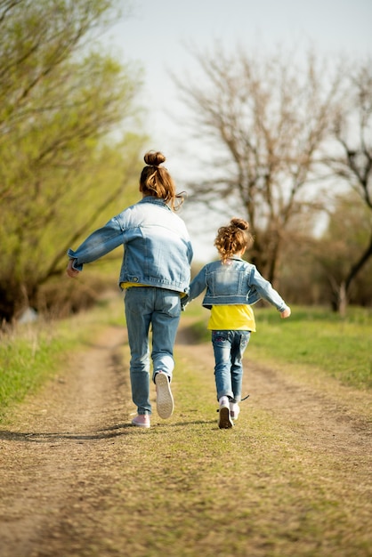 写真 2人のかわいい姉妹の女の子が空の田舎道を走っています春の自由子供時代の家族