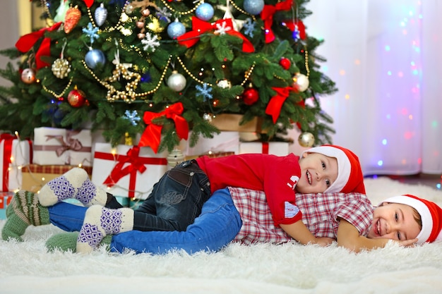 2人のかわいい小さな兄弟がクリスマスの装飾の背景にカーペットの上に横たわっています