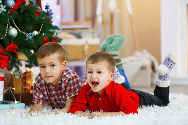 Two cute small brothers lie on carpet on Christmas tree background