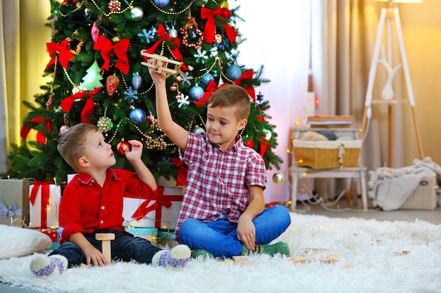 Two cute small brothers playing with wooden plane on Christmas tree