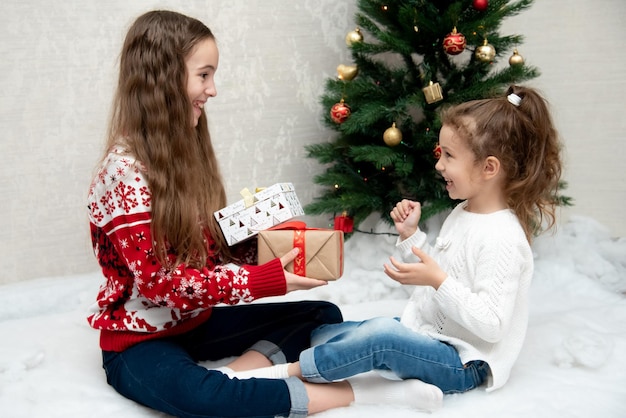 2 人のかわいい笑顔の女の子がクリスマス ツリーの隣に座って、お互いに贈り物をします。新年。クリスマス。