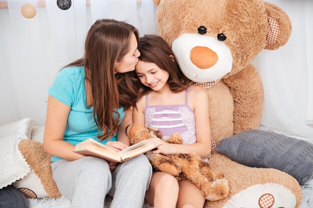 Two cute smiling sisters reading and kissing in children room