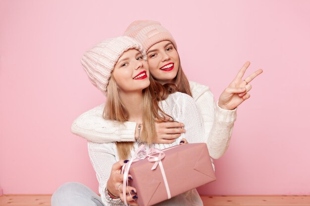 Two cute woman with red lips and hats giving gifts for a holiday and making peace