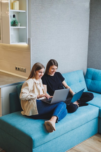 Two cute women are chatting with their friends via video call\
using a laptop in the living room friends friendship time together\
girlfriends are sitting on the couch and watching a movie