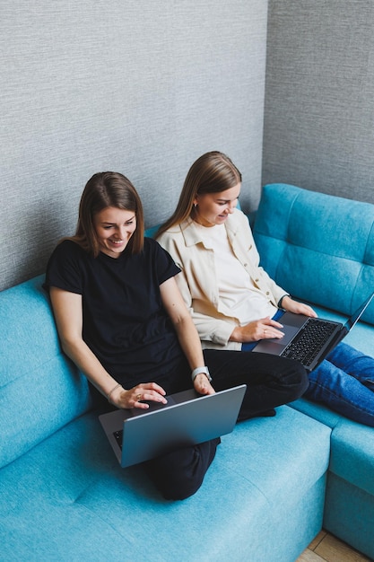 Two cute women are chatting with their friends via video call\
using a laptop in the living room friends friendship time together\
girlfriends are sitting on the couch and watching a movie